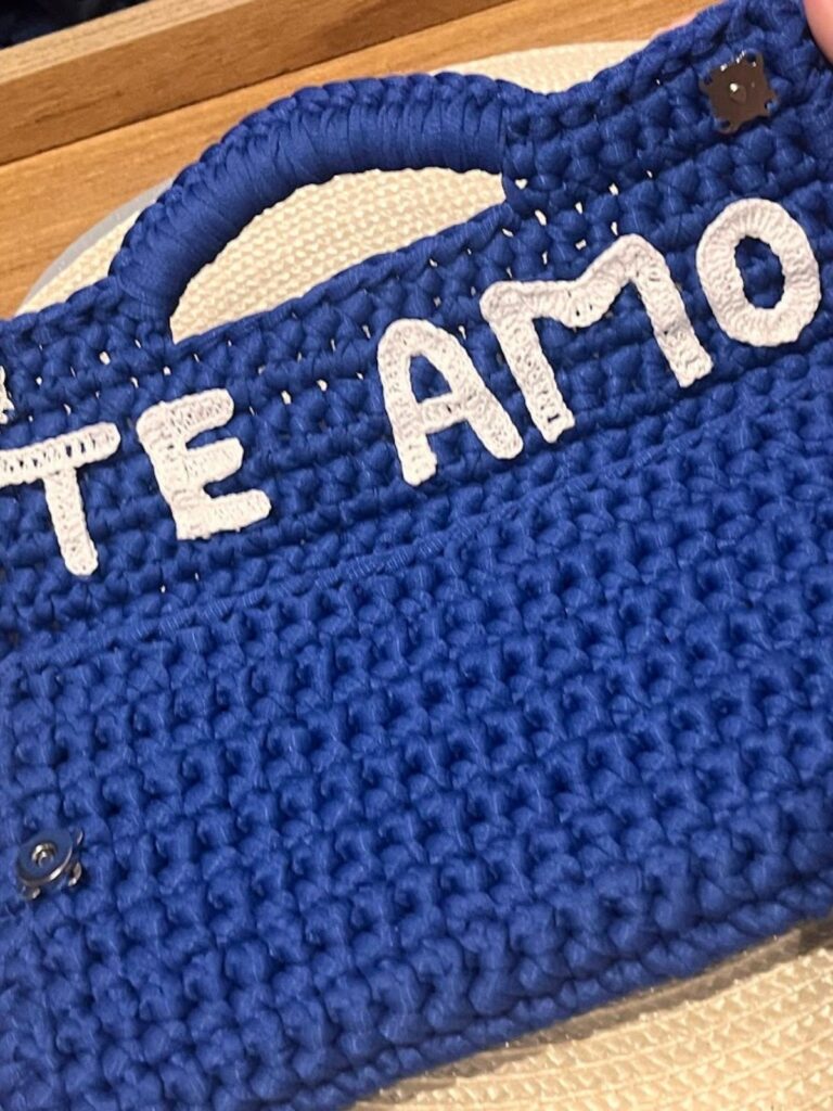 Capa da Receita Clutch de Crochê Enlace em PDF, mostrando modelo segurando a bolsa azul royal estruturada com selo de PDF gratuito. - eu te amo